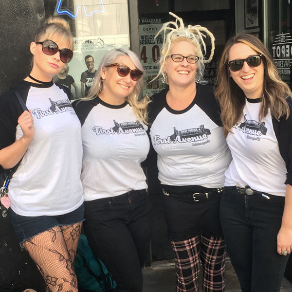 Group of people wearing a white baseball tee with 3/4 length black sleeves. Retro First Avenue logo on front in black screenprint.