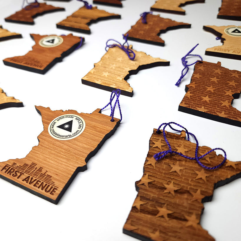 Wooden ornaments shaped like Minnesota with engraved First Avenue logo on the back, and stars/brick design on the front