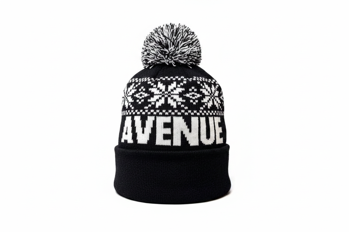 First Avenue Snowflake Pom hat - a black knit hat with white snowflakes and "FIRST AVENUE" with a black and white pom pom on the top.