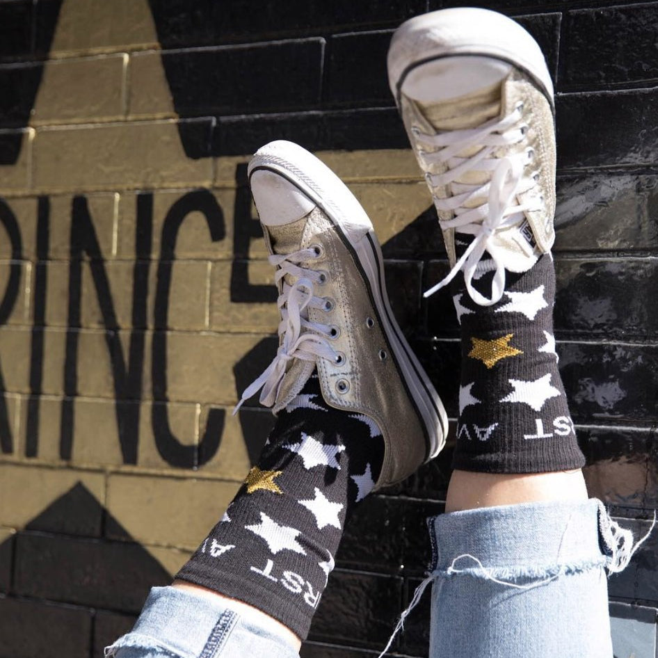 Black First Avenue x Hippy Feet Socks featuring gold and white stars and "First Avenue" in white at the top of each sock.